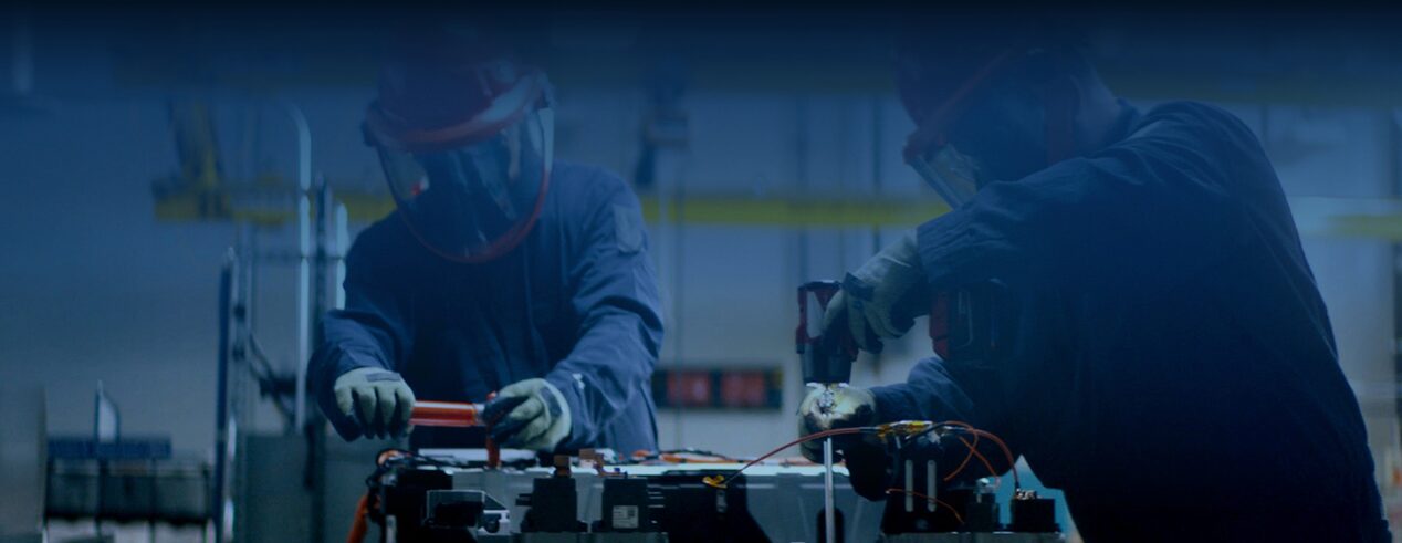 Two Men in a Darkly Lit Warehouse Fixing a Vehicle Part